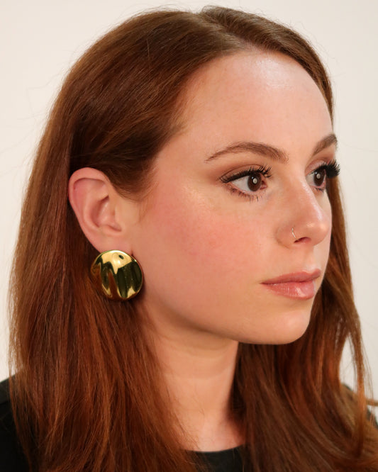 Close-up of a woman wearing gold earrings with a plain background