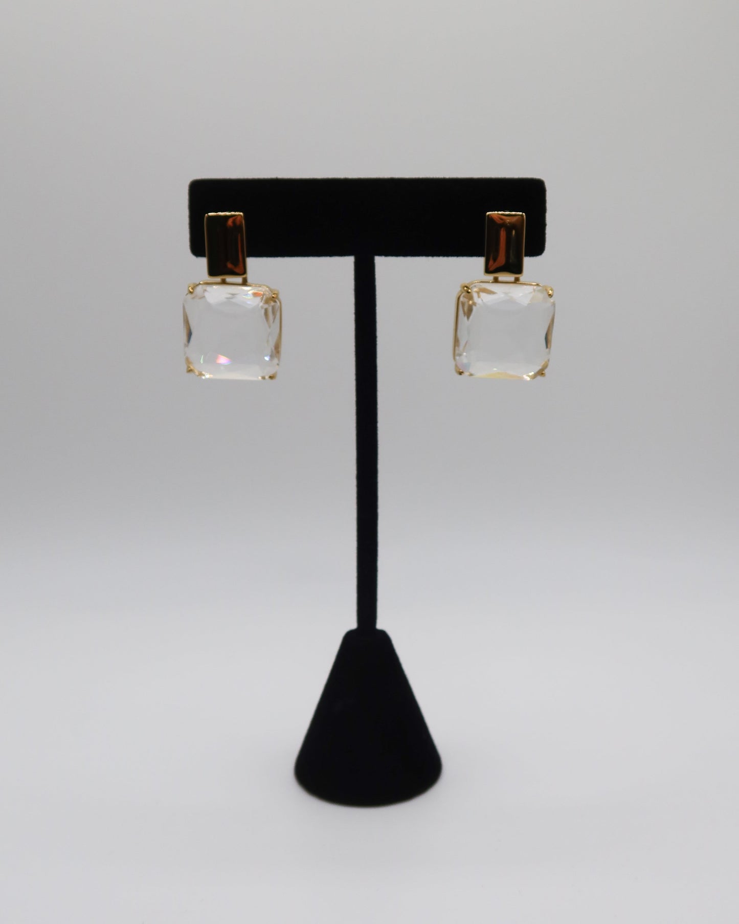 Square earrings on a black earring stand against a gray background