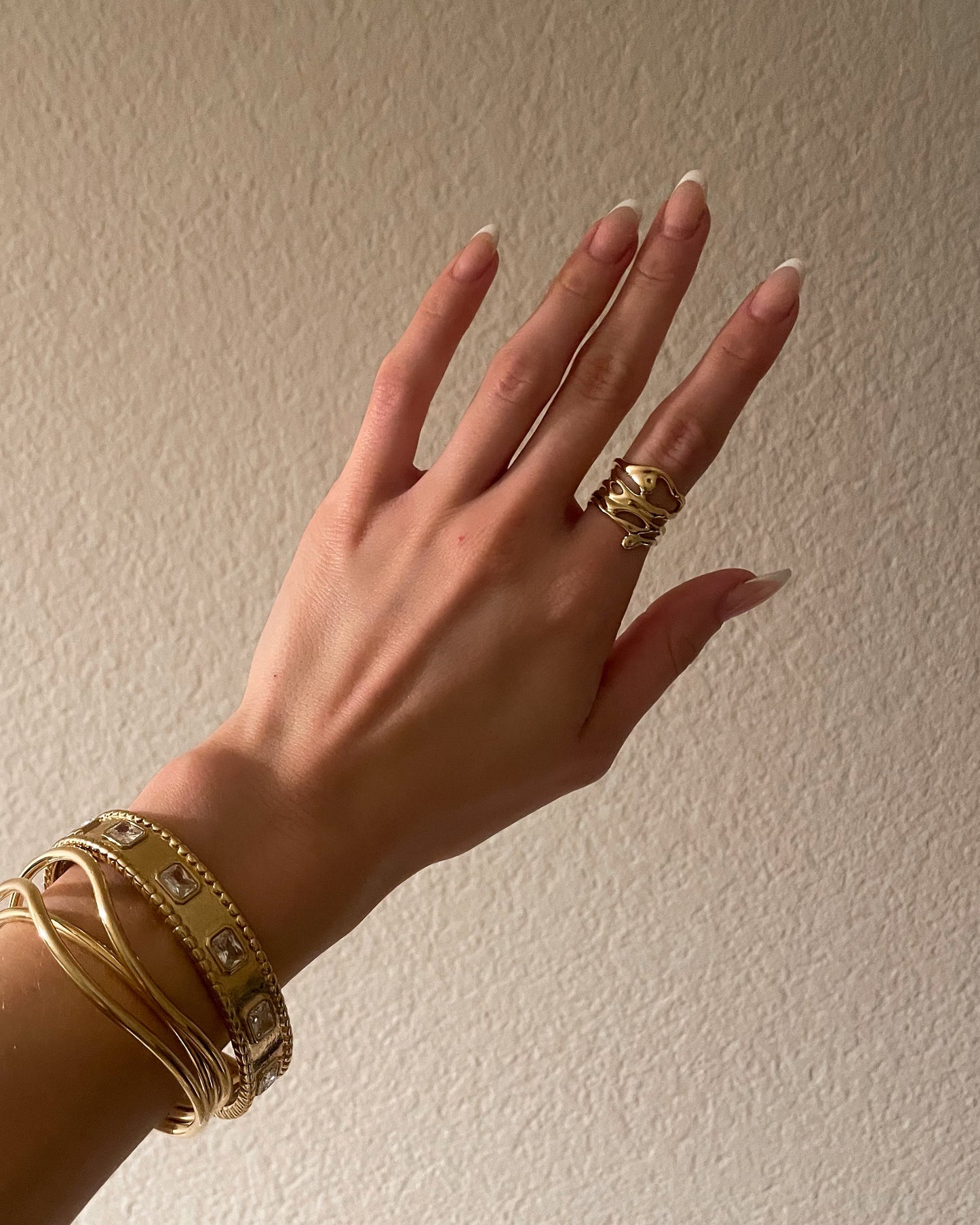 Hand wearing gold jewelry against a plain background
