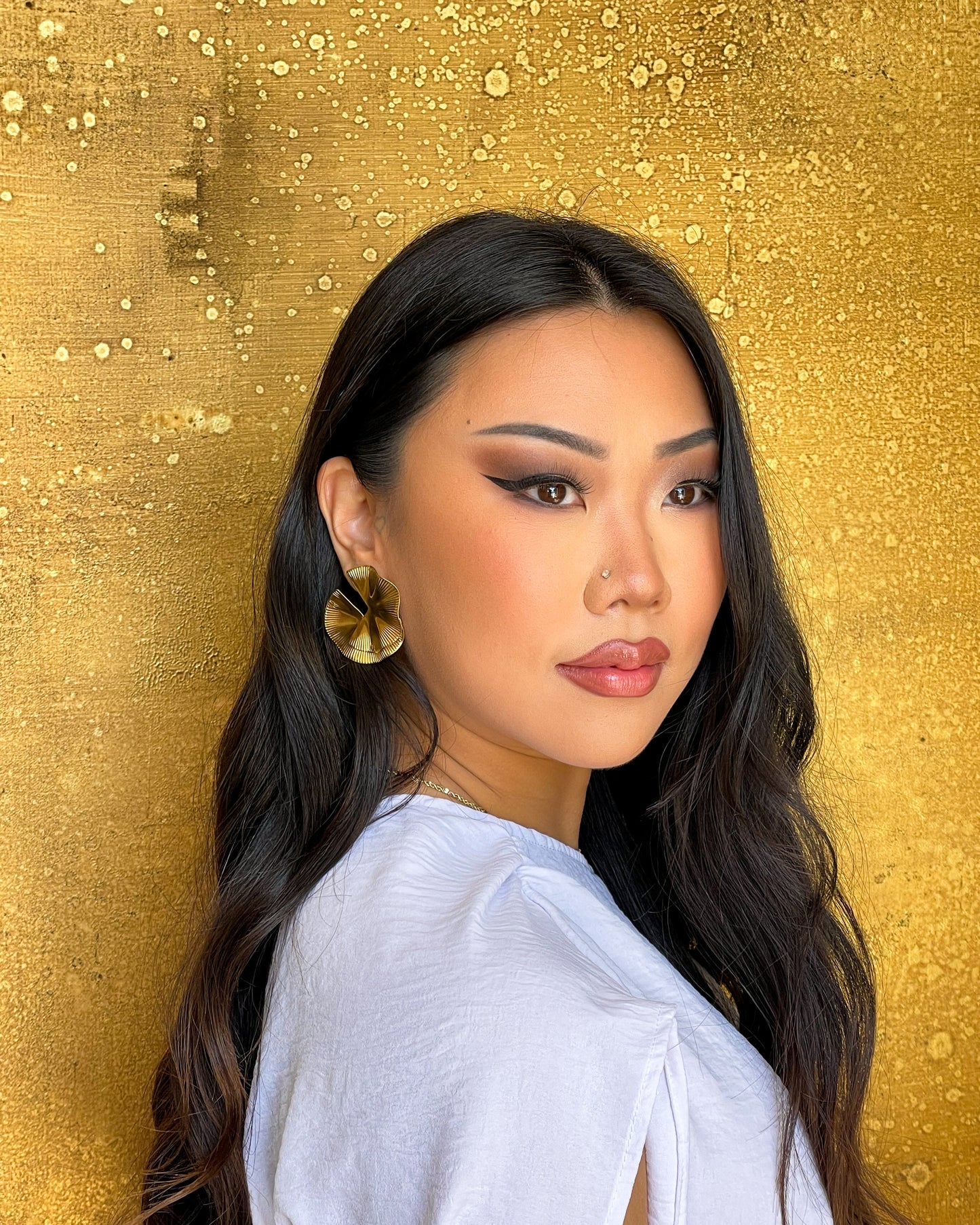 Woman with long dark hair and gold earrings against a gold textured background