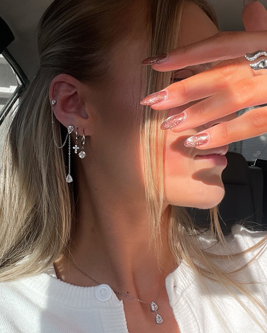 Close-up of a person wearing earrings and a necklace, with a hand covering the camera.