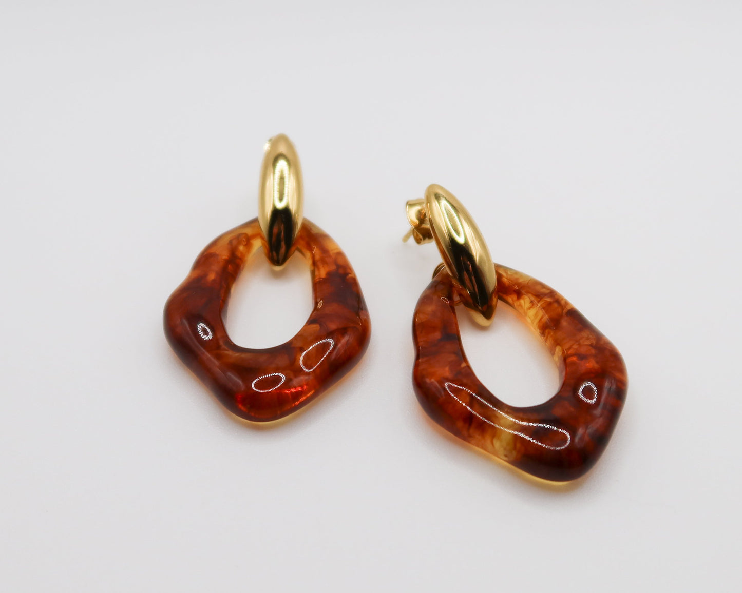 Pair of amber hoop earrings with gold hooks on a light gray background