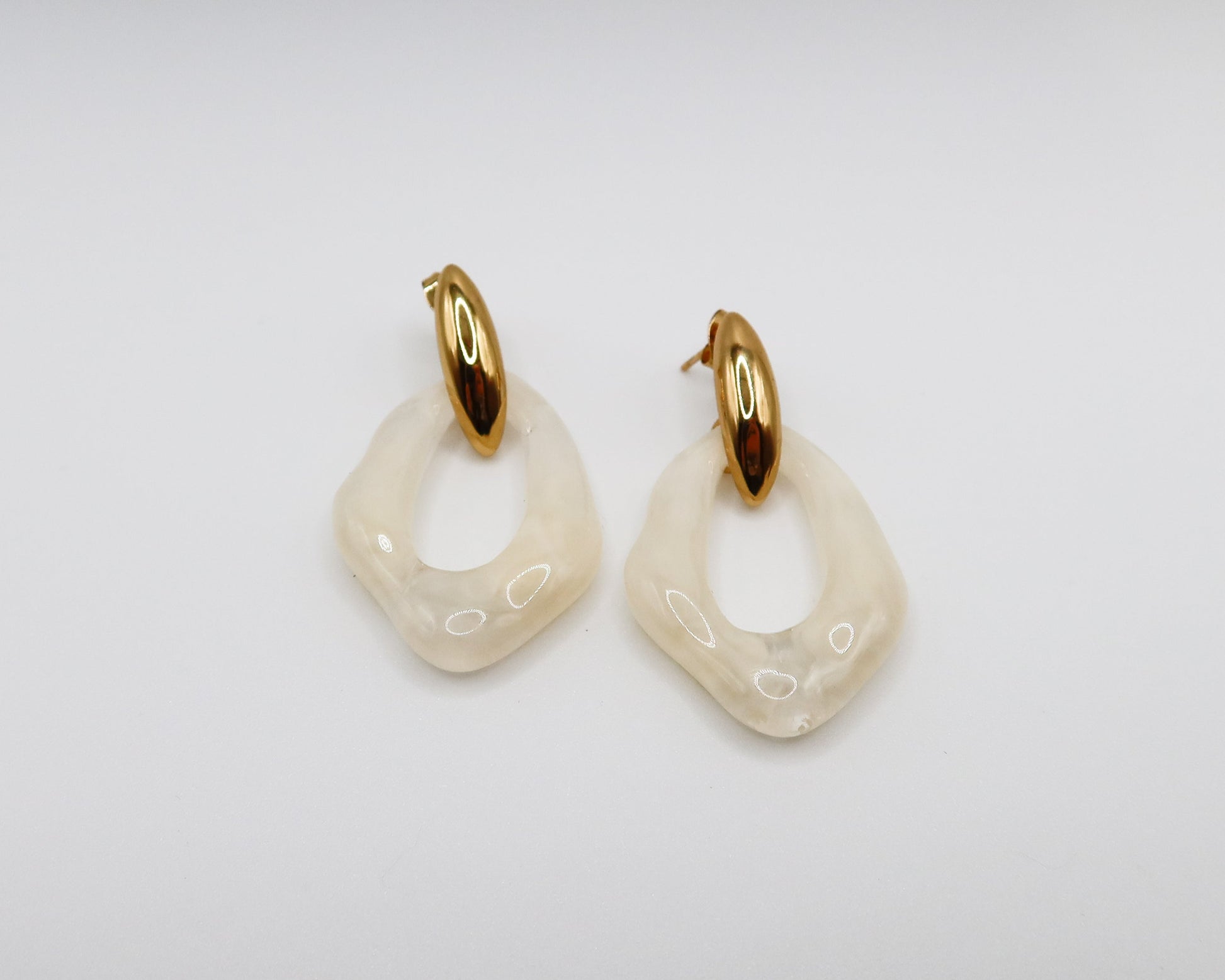Pair of gold and white hoop earrings on a light gray background