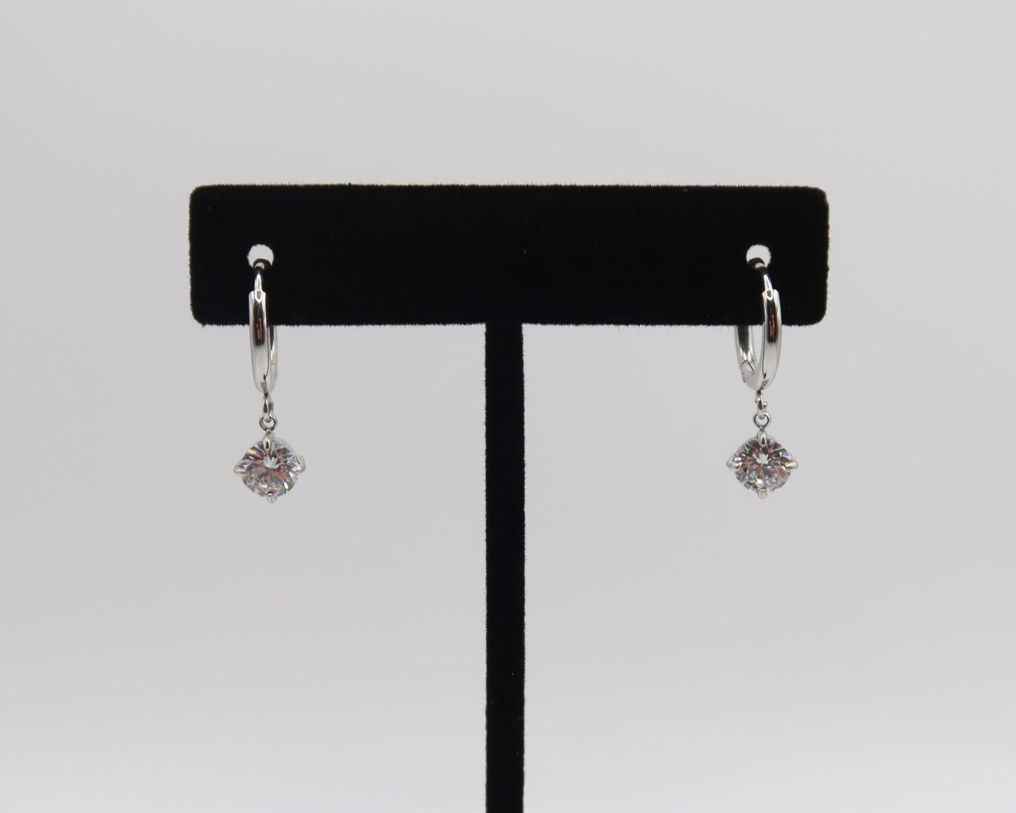 Pair of silver earrings on a black earring stand against a white background