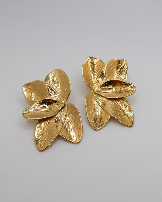 Pair of gold flower-shaped earrings on a gray background