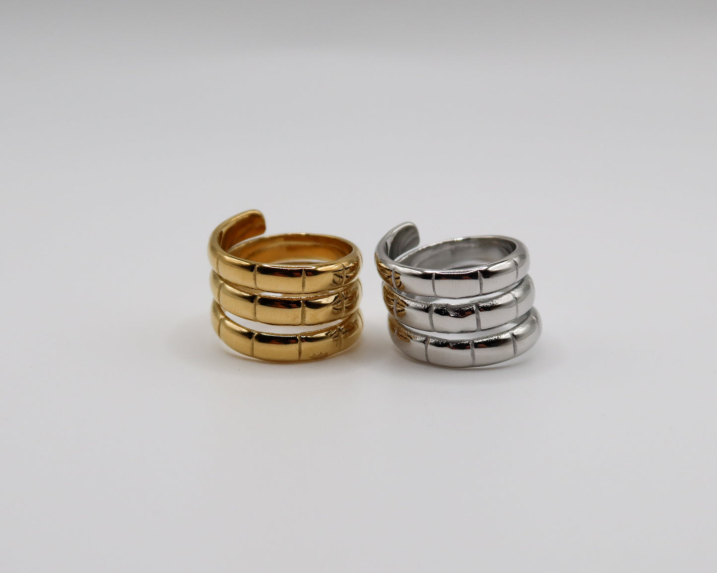Two spiral-shaped rings, one gold and one silver, on a light gray background.