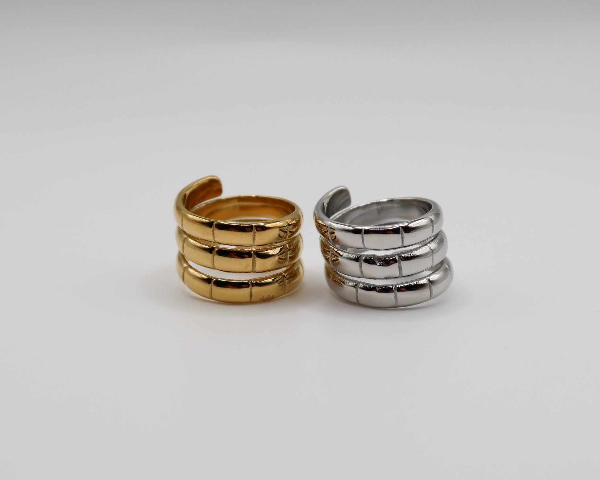 Two spiral-shaped rings, one gold and one silver, on a light gray background.