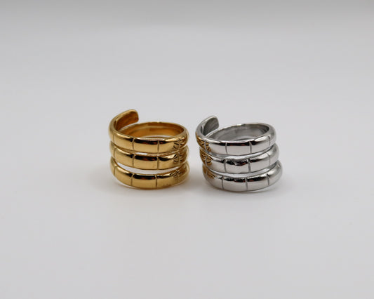 Two spiral-shaped rings, one gold and one silver, on a light gray background.