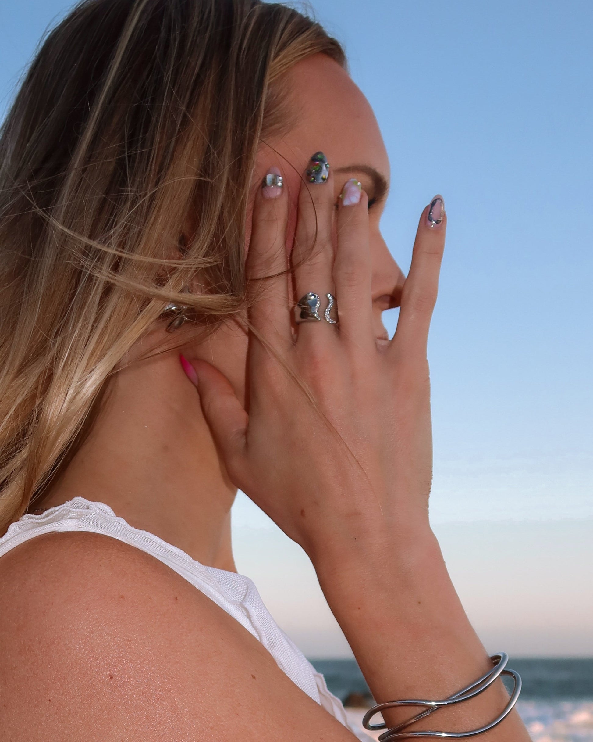 Woman with multiple rings and bracelets on a blurred beach background
