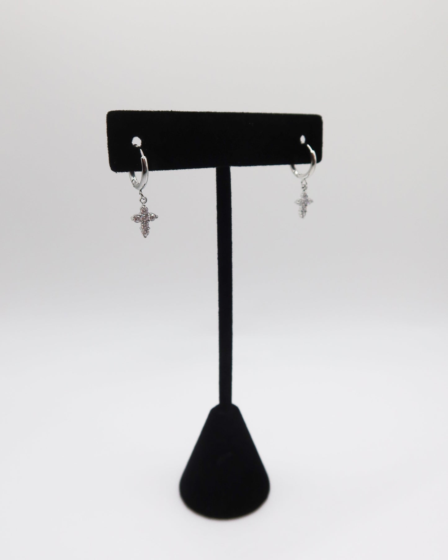 Pair of silver cross earrings on a black earring stand against a white background