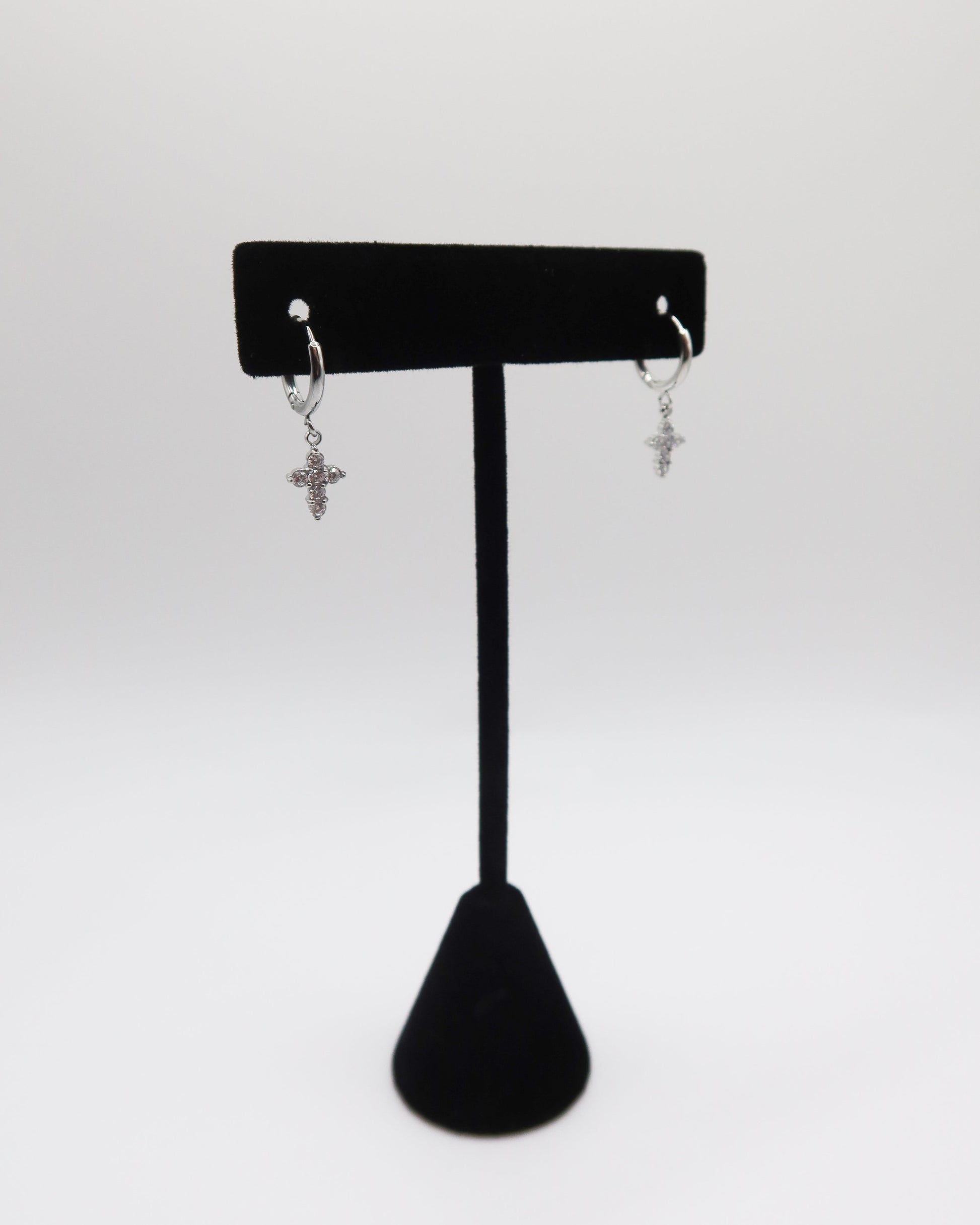 Pair of silver cross earrings on a black earring stand against a white background