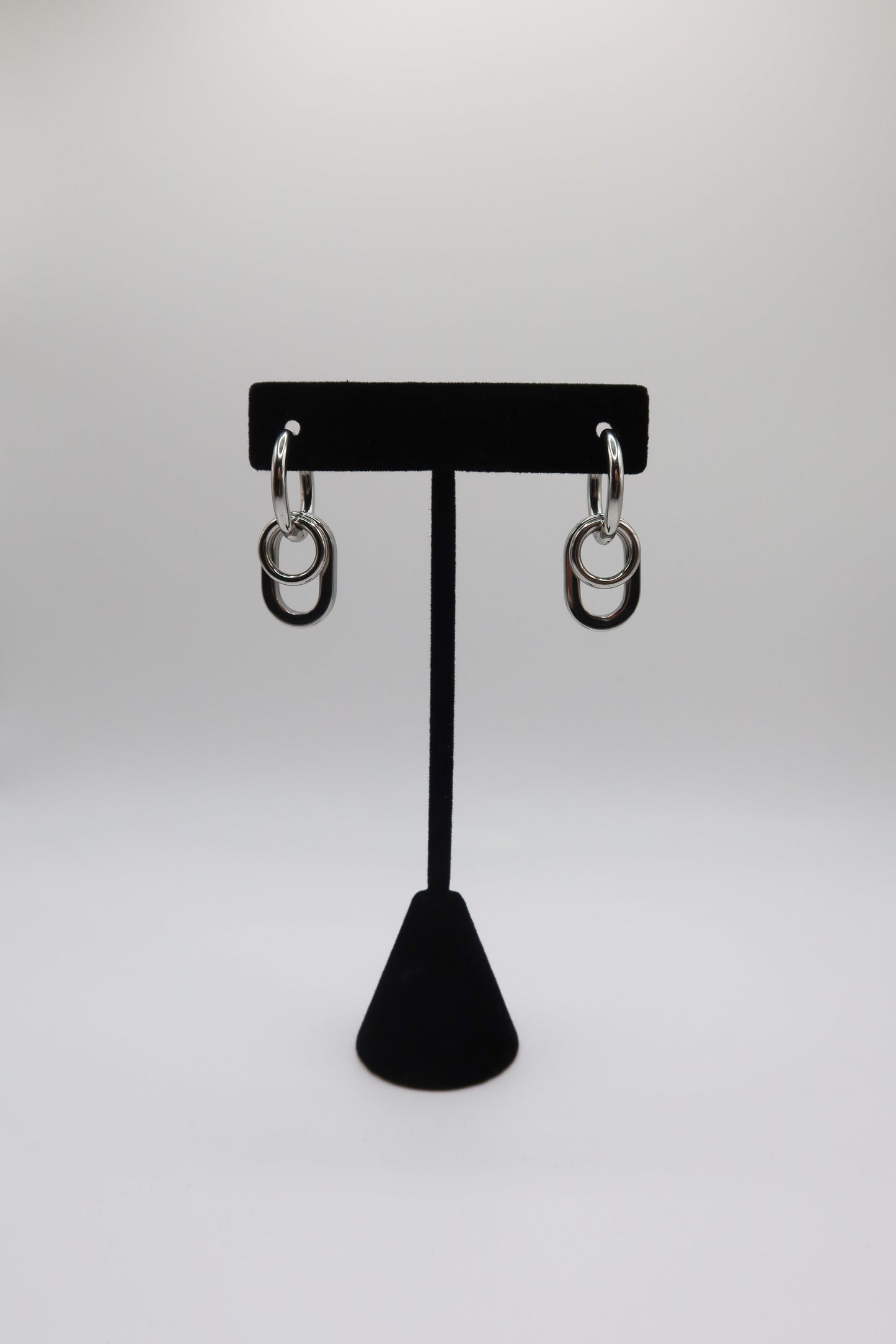 Pair of silver hoop earrings on a black earring stand against a white background
