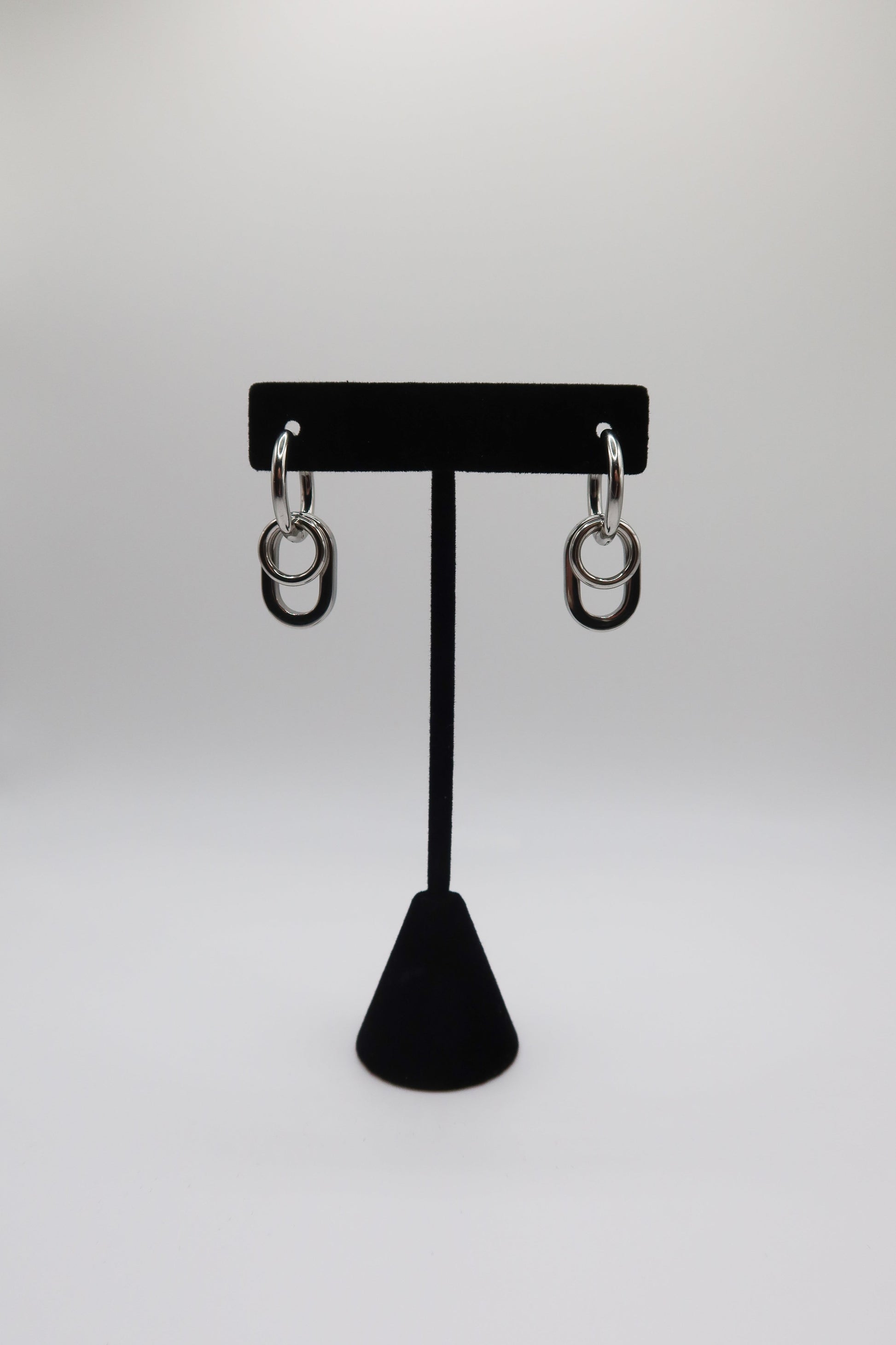 Pair of silver hoop earrings on a black earring stand against a white background