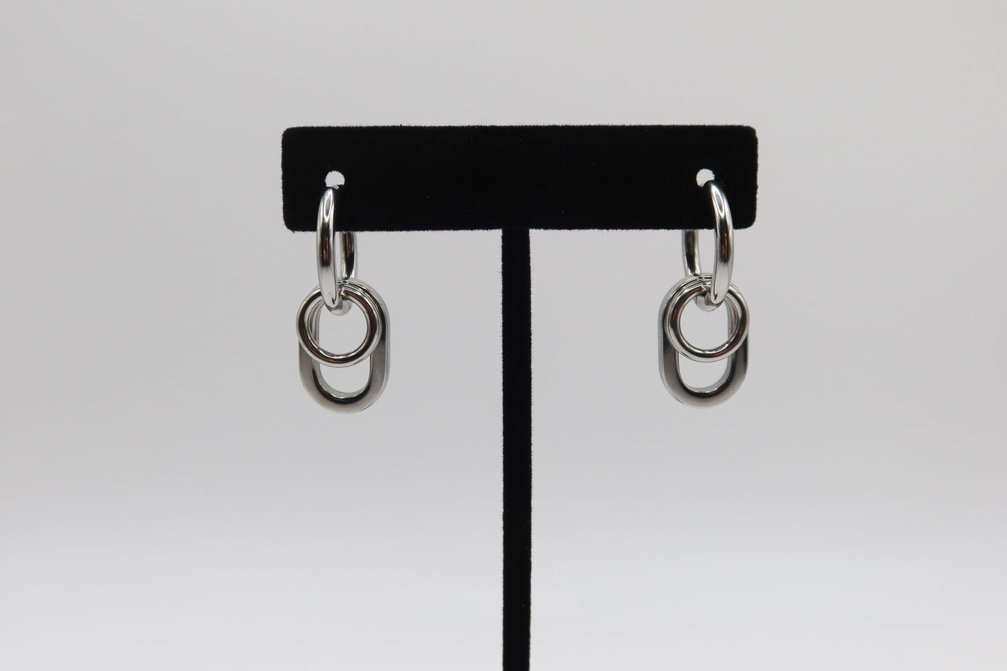 Pair of silver hoop earrings on a black earring stand against a white background