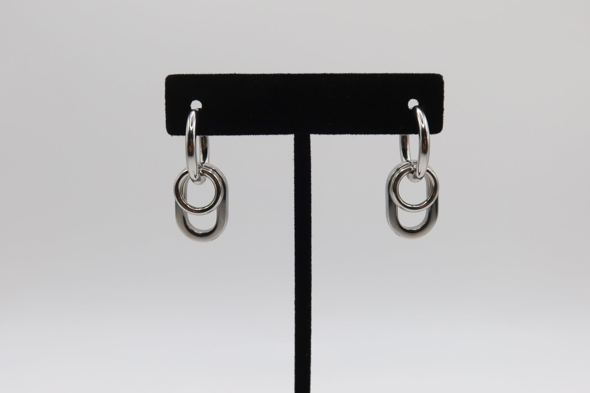 Pair of silver hoop earrings on a black earring stand against a white background