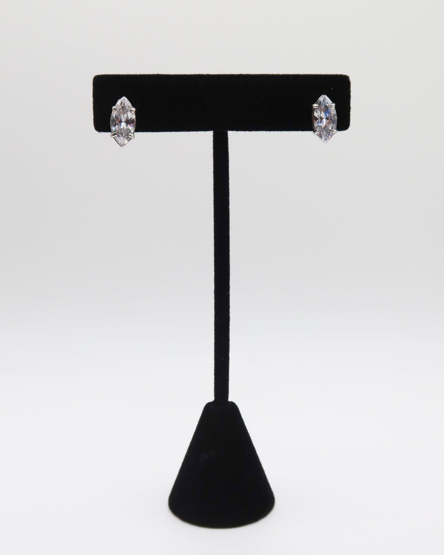 Black T-shaped earring stand with two silver earrings on a white background