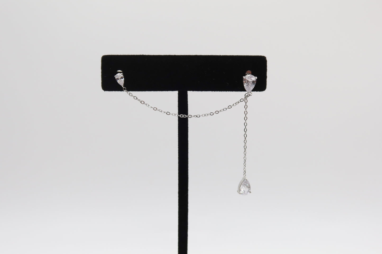 Pair of silver earrings on a black stand against a white background