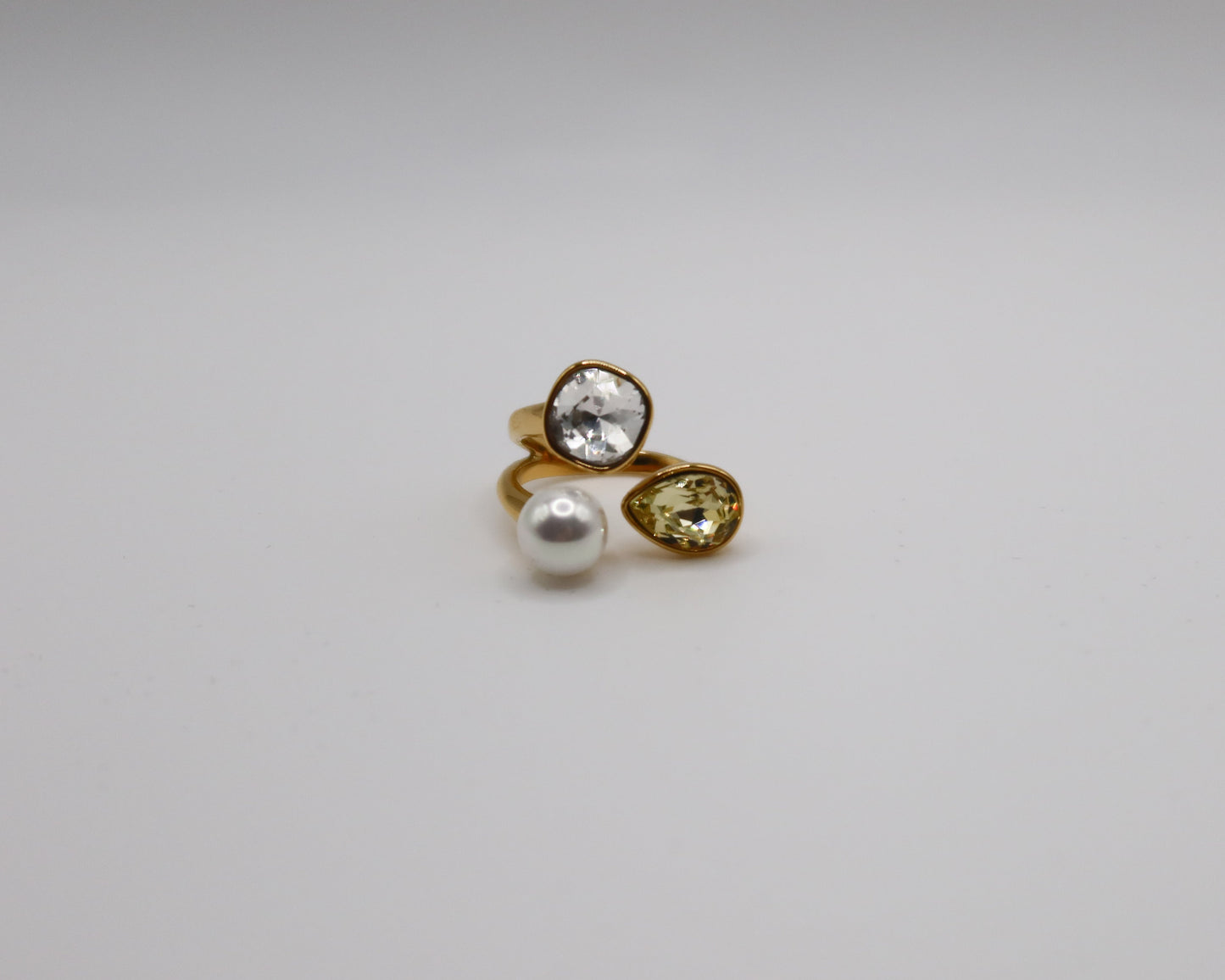 Gold ring with a pearl and pear-shaped gemstone on a white background