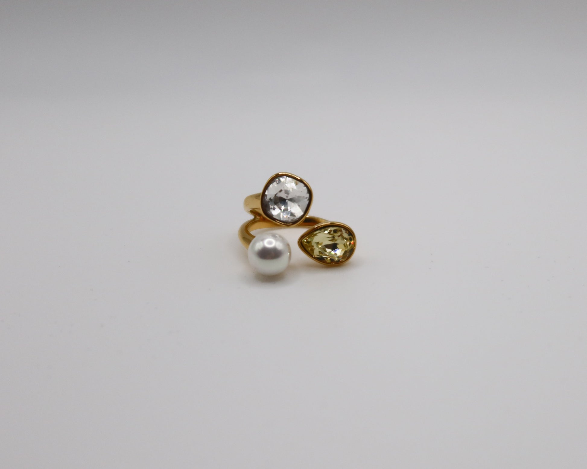 Gold ring with a pearl and pear-shaped gemstone on a white background
