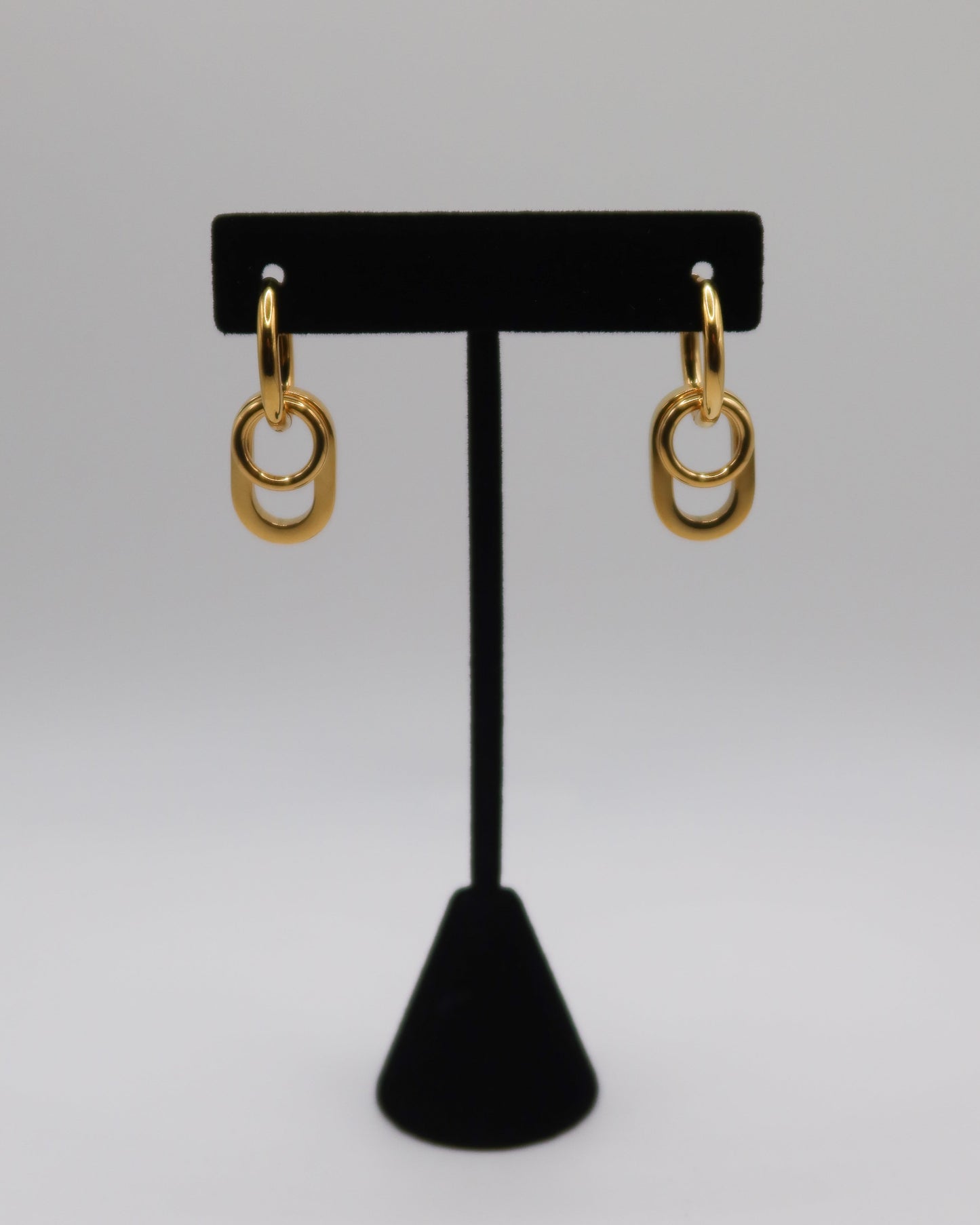 Gold hoop earrings on a black earring stand against a gray background