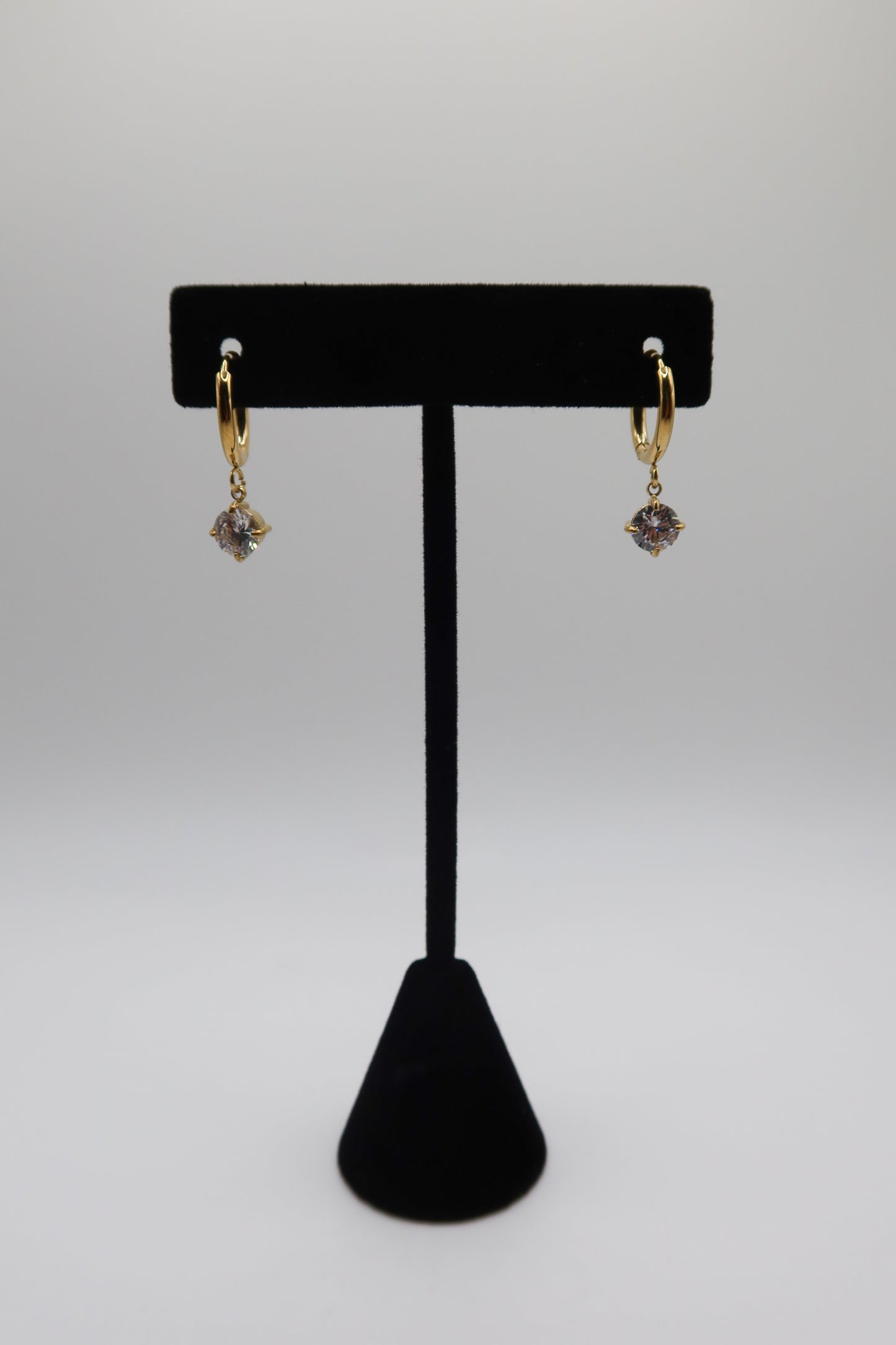 Gold earrings with purple stones on a black earring stand against a white background