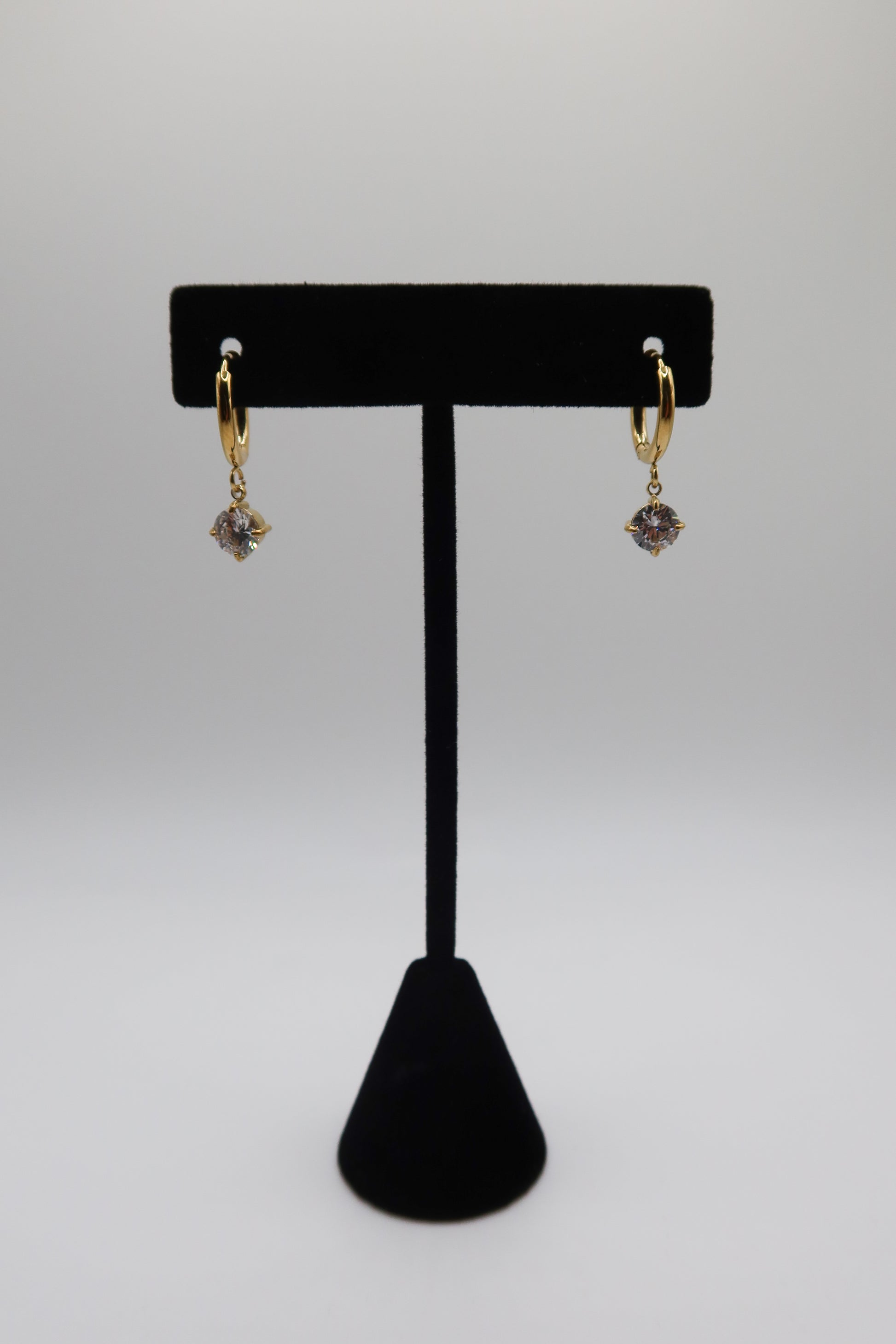 Gold earrings with purple stones on a black earring stand against a white background