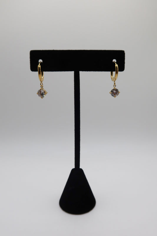 Gold earrings with purple stones on a black earring stand against a white background
