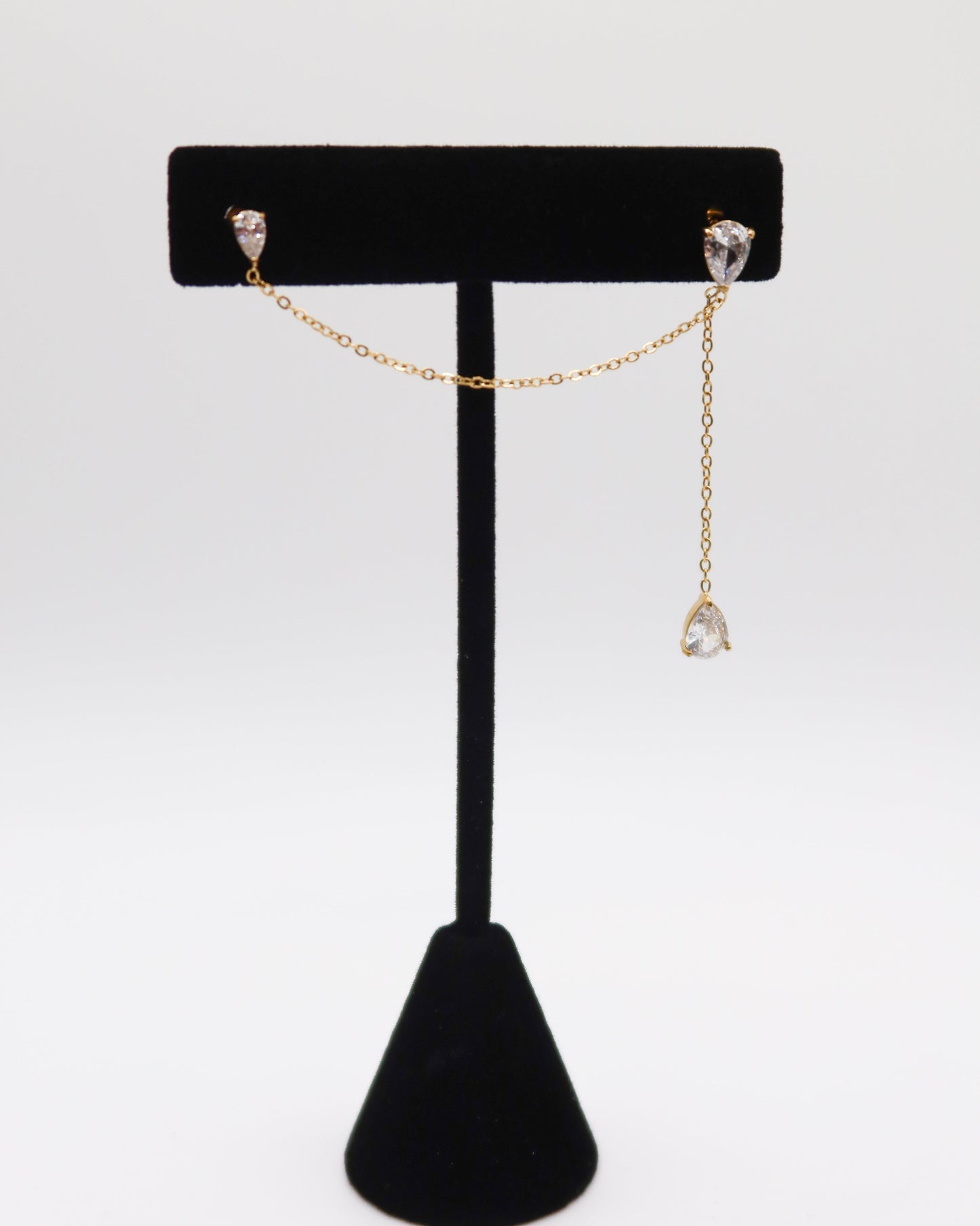 Gold chain earring on a black jewelry stand against a white background