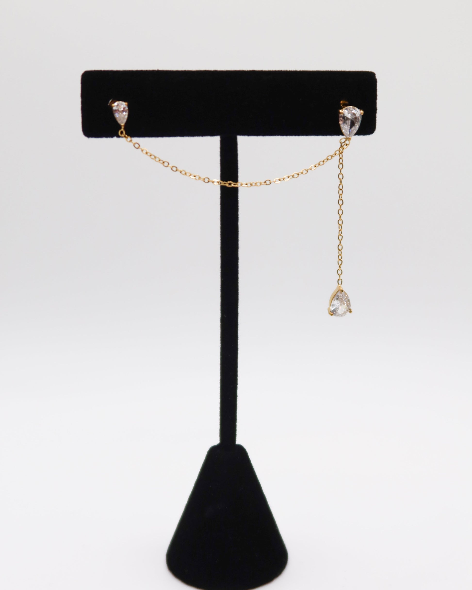 Gold chain earring on a black jewelry stand against a white background