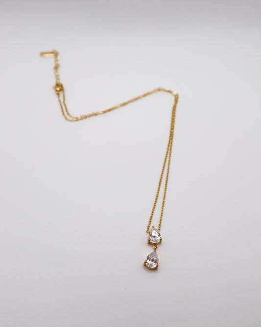 Gold necklace with pear-shaped pendant on a light gray background