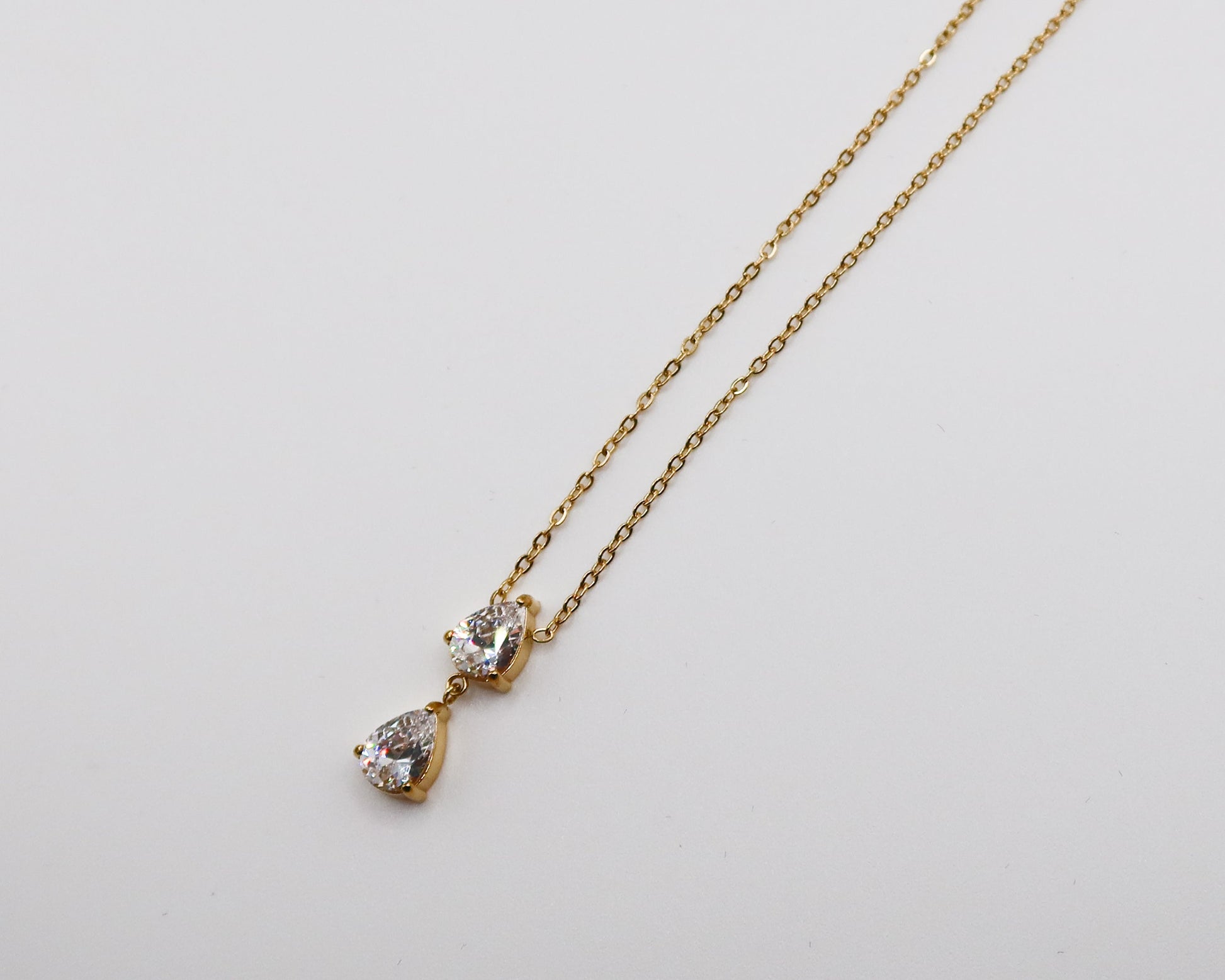 Gold necklace with a teardrop-shaped pendant on a light gray background