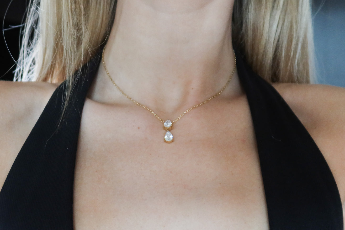 Gold necklace with a pendant on a person wearing a black top.
