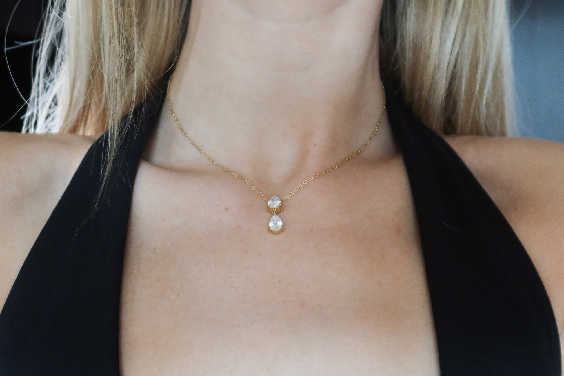 Gold necklace with a pendant on a person wearing a black top.