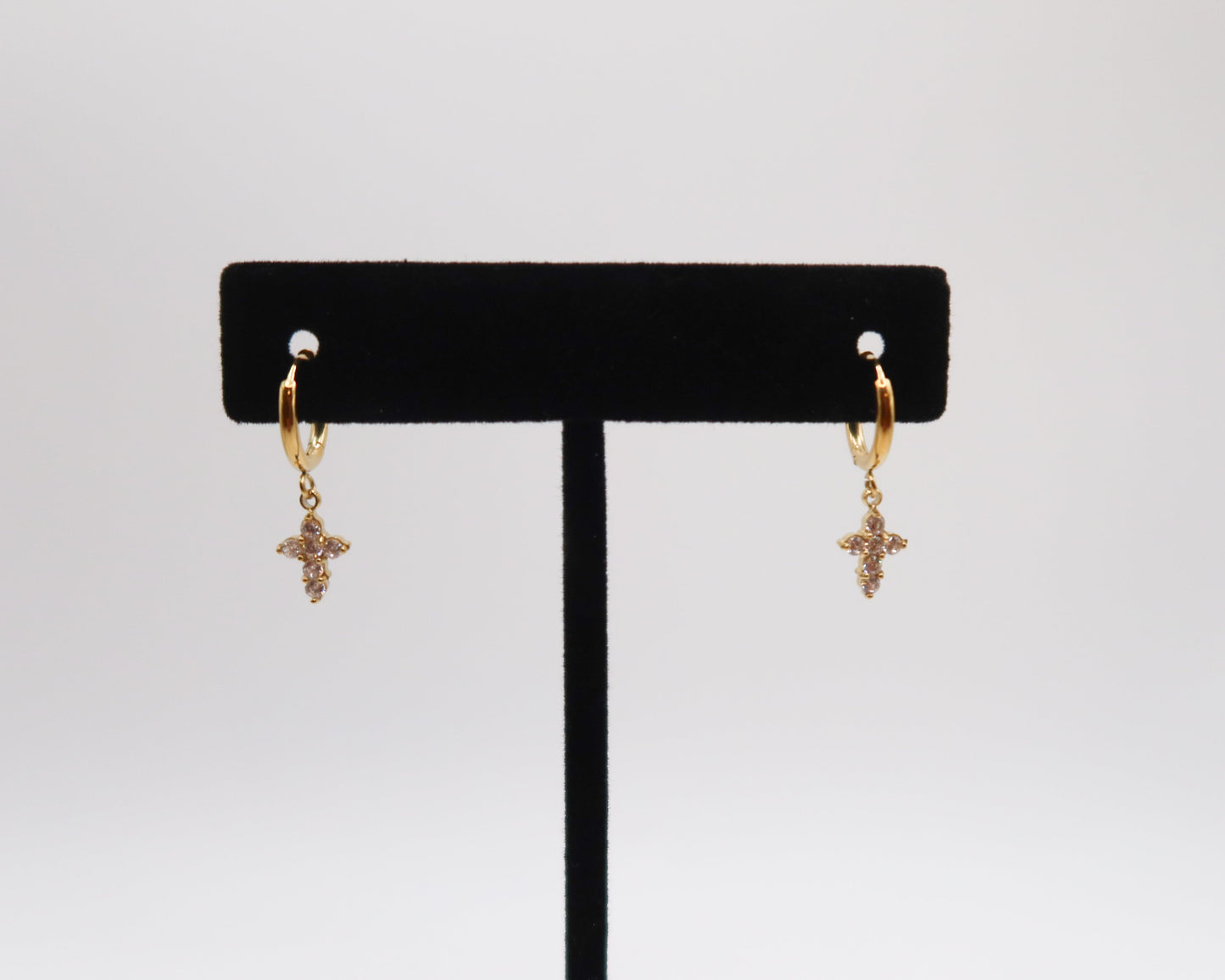 Gold cross earrings on a black earring stand against a white background