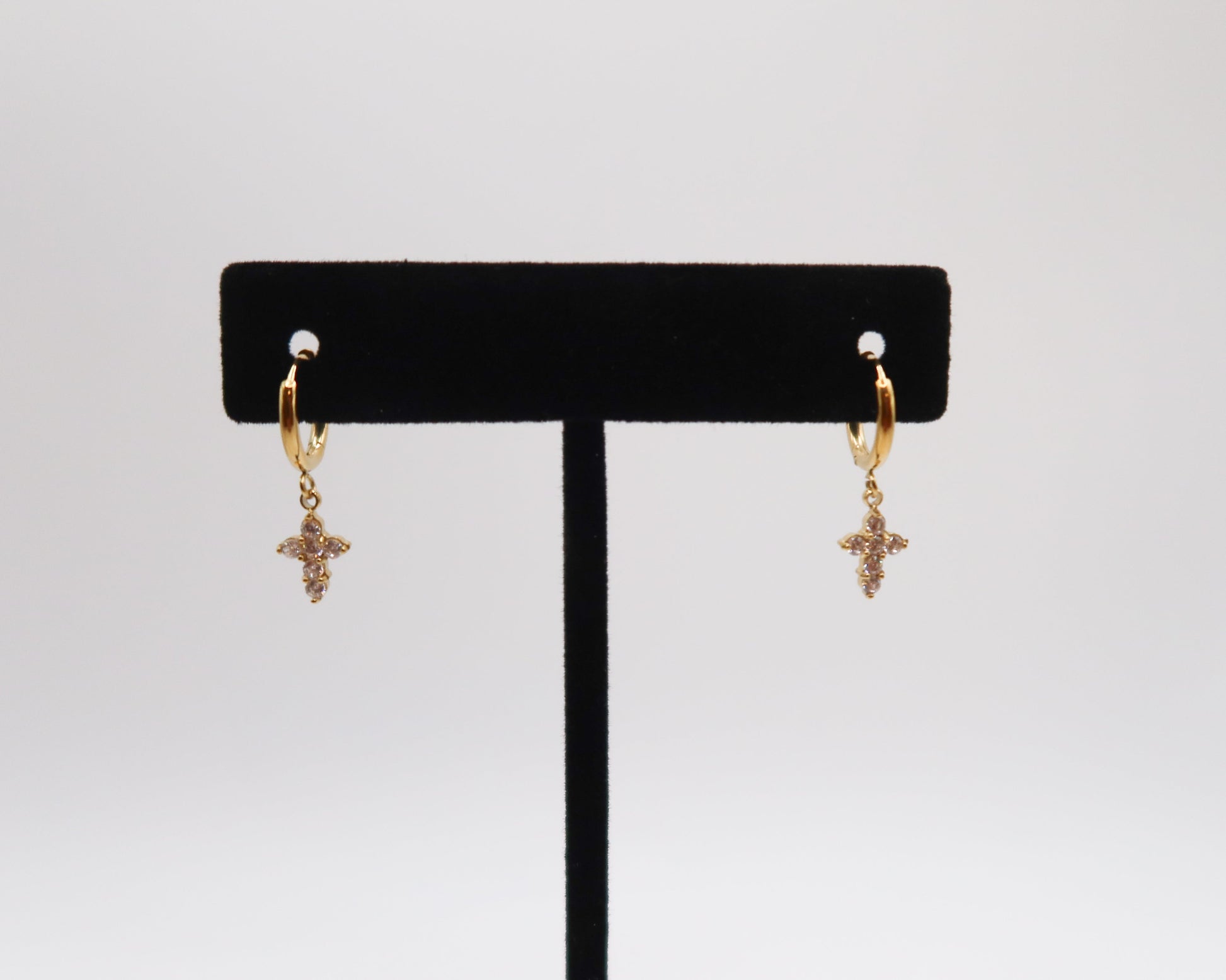 Gold cross earrings on a black earring stand against a white background