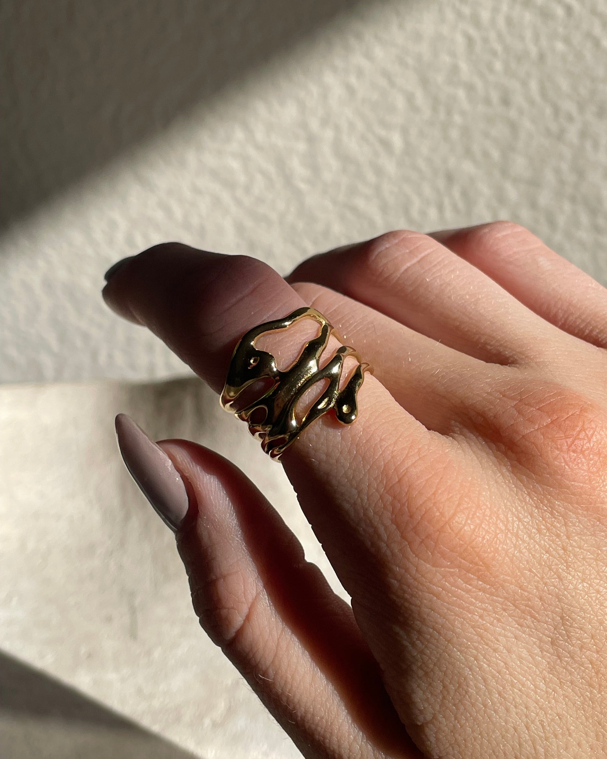 Hand wearing a gold ring with a textured design on a neutral background