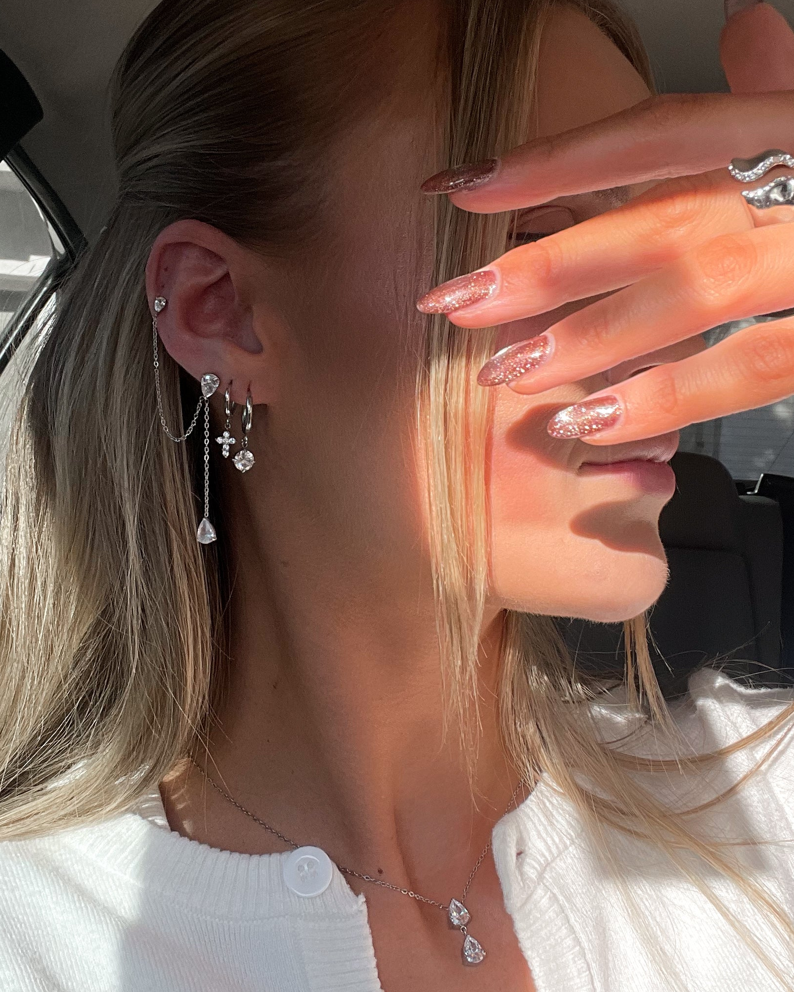Close-up of a person wearing earrings and a necklace, with a hand covering the camera.