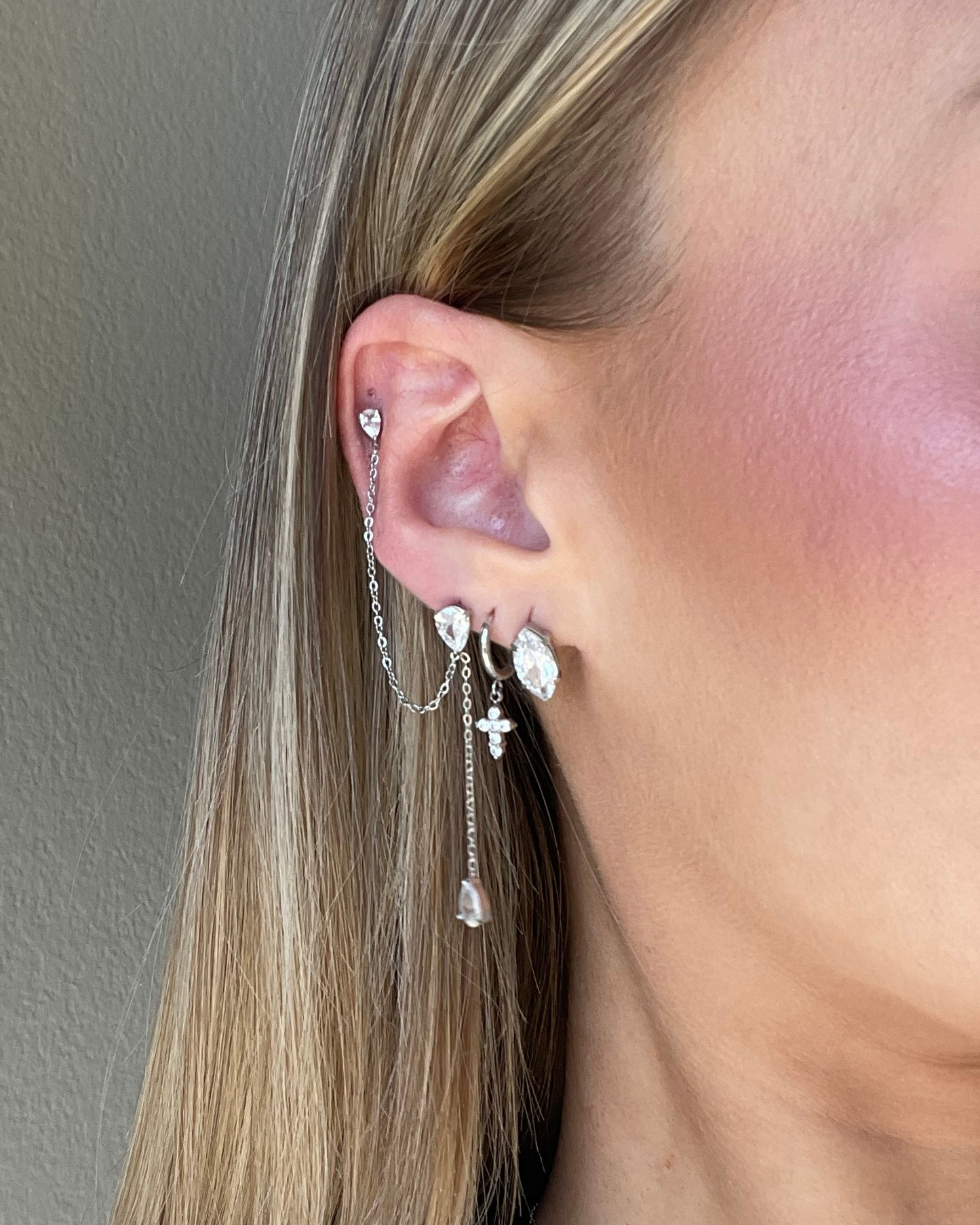 Close-up of an ear with silver earrings against a neutral background