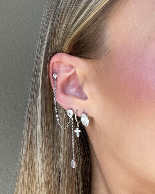 Close-up of an ear with silver earrings against a neutral background