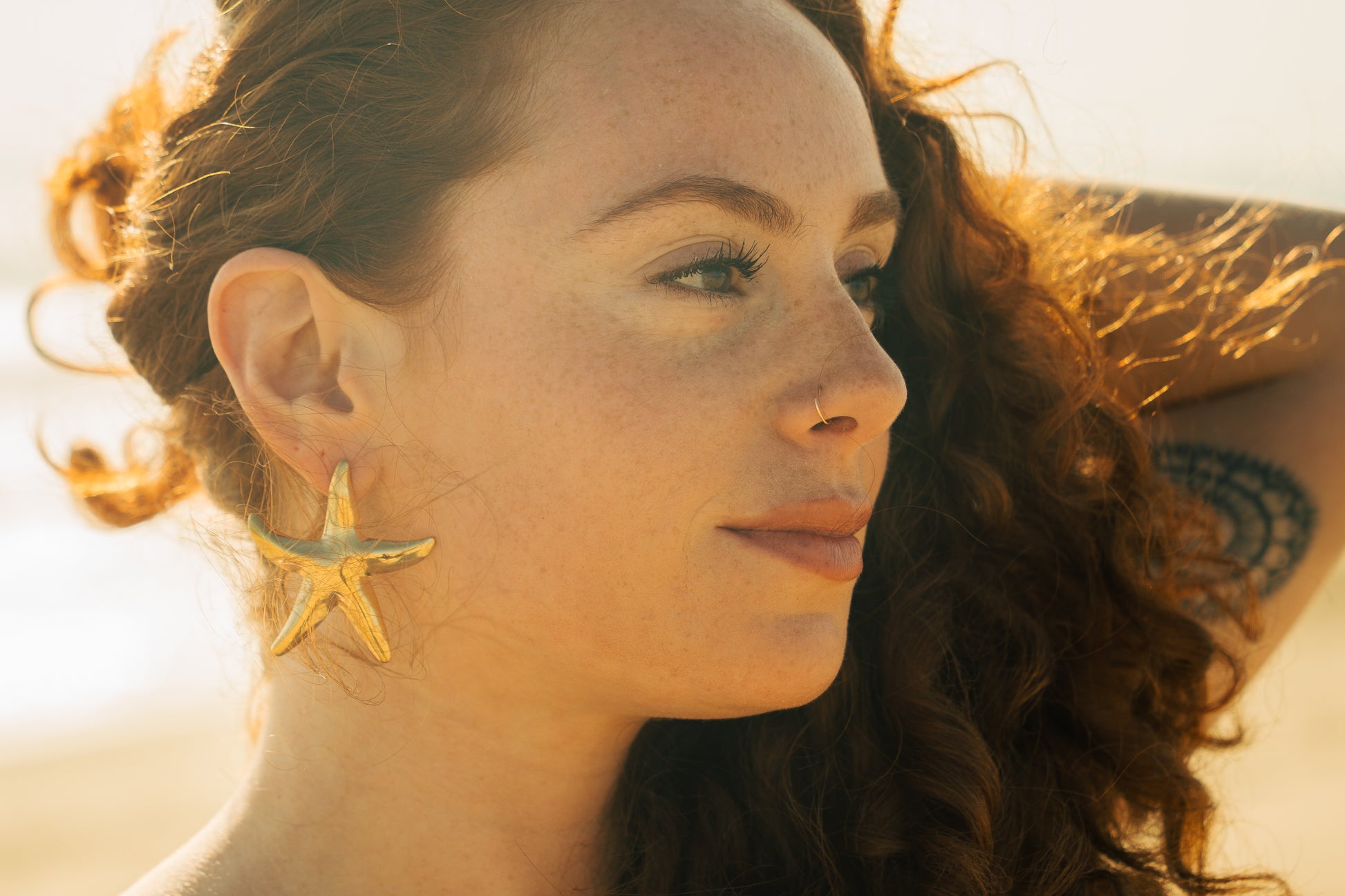 Close-up of a woman wearing gold starfish earrings with a blurred background