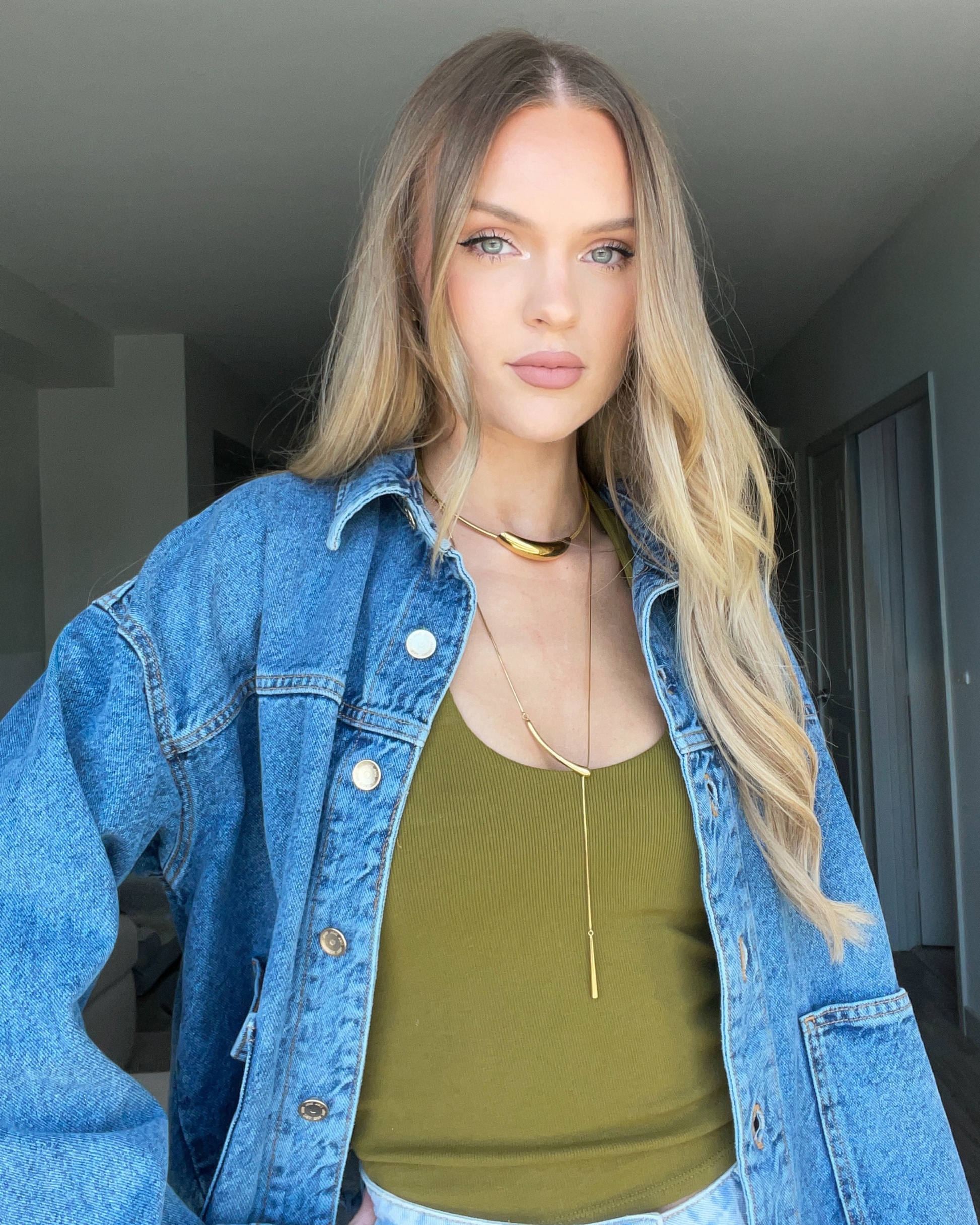 Close-up of a person wearing a blue denim jacket with a gold necklace.